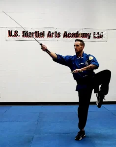 A 2nd degree Black Sash, is wielding 2 straight swords while balancing on one foot at US Martial Arts Academy Black Sash-test forms. Learning Self-defense and improving fitness, focus, fitness, strength, self-discipline, balance, confidence, and memory in Kung Fu and Tai Chi in class at US Martial Arts Academy Ltd in Cockeysville Maryland 21030 www.usmaltd.com; 410-561-9882