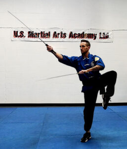 2nd degree Black Sash, wielding 2 straight swords while balancing on one foot at US Martial Arts Academy Ltd. Learning Self-defense and improving fitness, focus, fitness, strength, self-discipline, balance, confidence, and memory in Kung Fu and Tai Chi in class in Cockeysville Maryland 21030 www.usmaltd.com; 410-561-9882