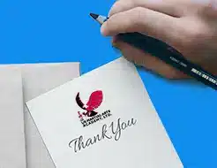 Hand holding a pen writing on a thank you card graphic from gingerquip of pixabay.com and modified by US Martial Arts Academy, Ltd, for the 2026 USKSF International Championship Tournament.
